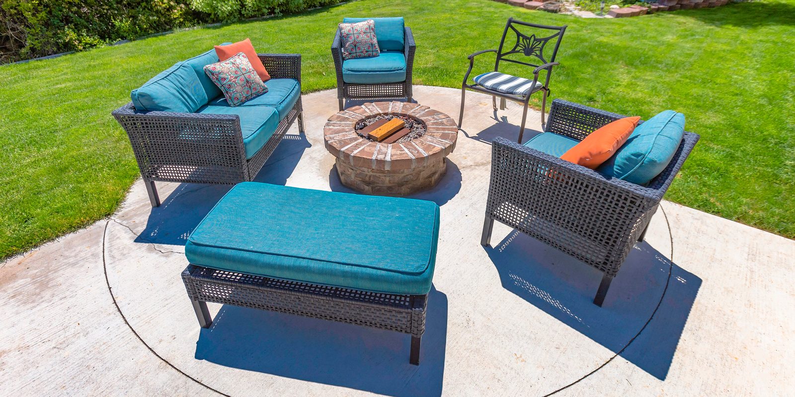 Circular gas fire pit on a concrete patio surrounded by wicker conversation seating